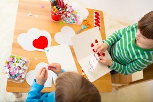 Kids children doing Valentine's day arts and crafts with hearts pencils paper